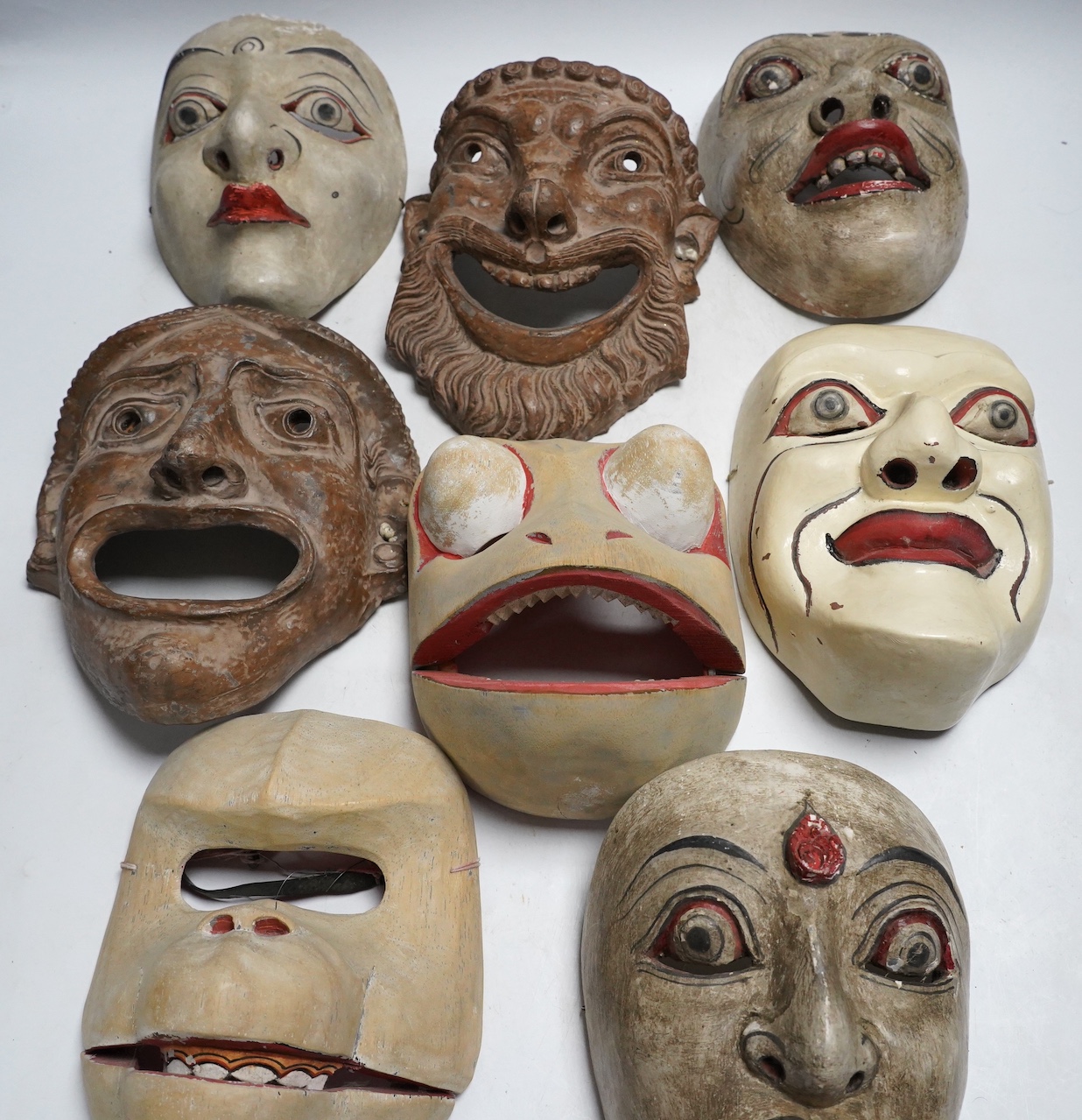 Two pottery face masks, and three pairs of carved and painted masks, largest mask 21cm high